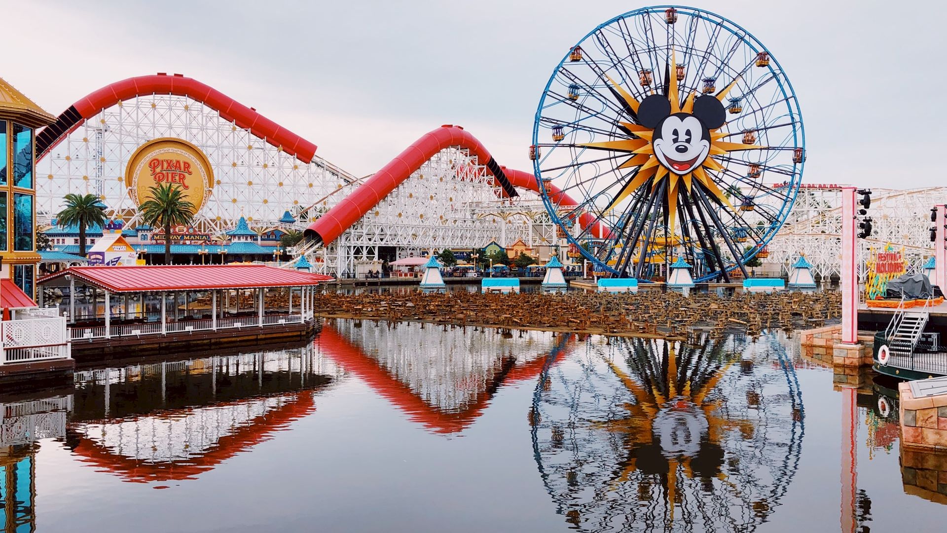 The image shows an amusement park with a large Ferris wheel featuring a familiar character, roller coasters, and water reflecting the rides.