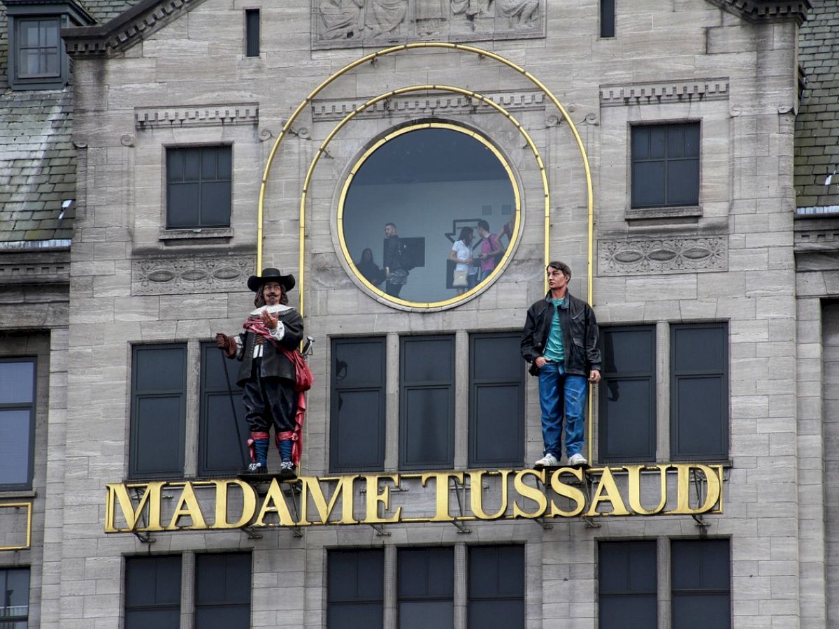 The image shows the exterior of the Madame Tussaud's museum, featuring two lifelike statues of figures above the entrance.