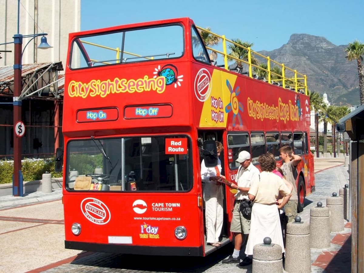 A red double-decker "City Sightseeing" bus with "Hop On, Hop Off" signs is parked, and people are standing near the entrance.