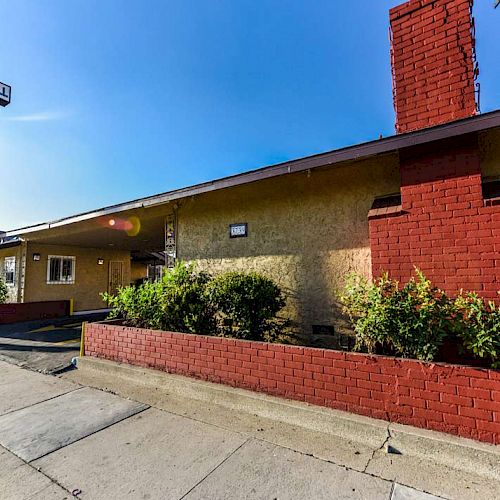 An exterior of a motel building with a red and white sign, red brick details, and some bushes in front.