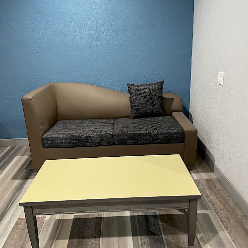 The image shows a small room with a sofa and a cushion against a blue wall, a coffee table with a yellow top, and a striped floor.