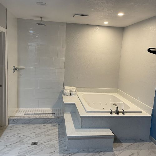 The image shows a modern bathroom with a walk-in shower and a large jetted bathtub, set against white and blue walls, and marble flooring.