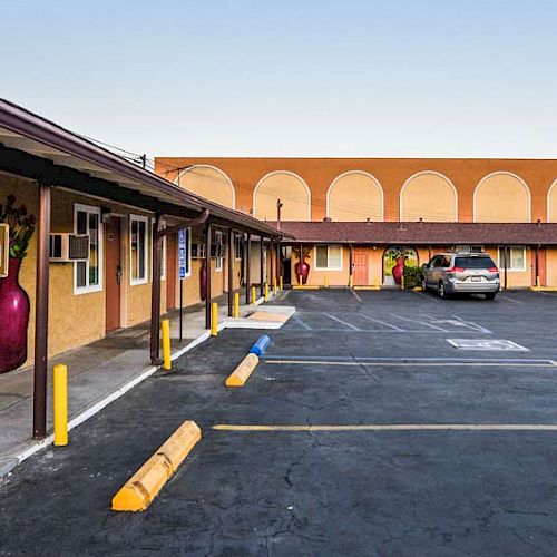 An outdoor view of a motel with parked cars, air conditioning units in windows, decorative wall art, and empty parking spaces in the foreground.