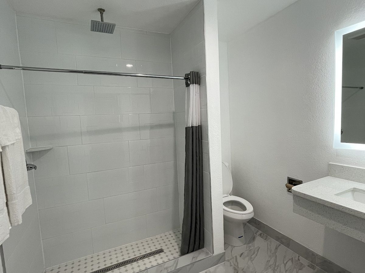 A modern bathroom with a glass-enclosed shower, a wall-mounted toilet, and a floating sink with a backlit mirror, features tiled walls and flooring.