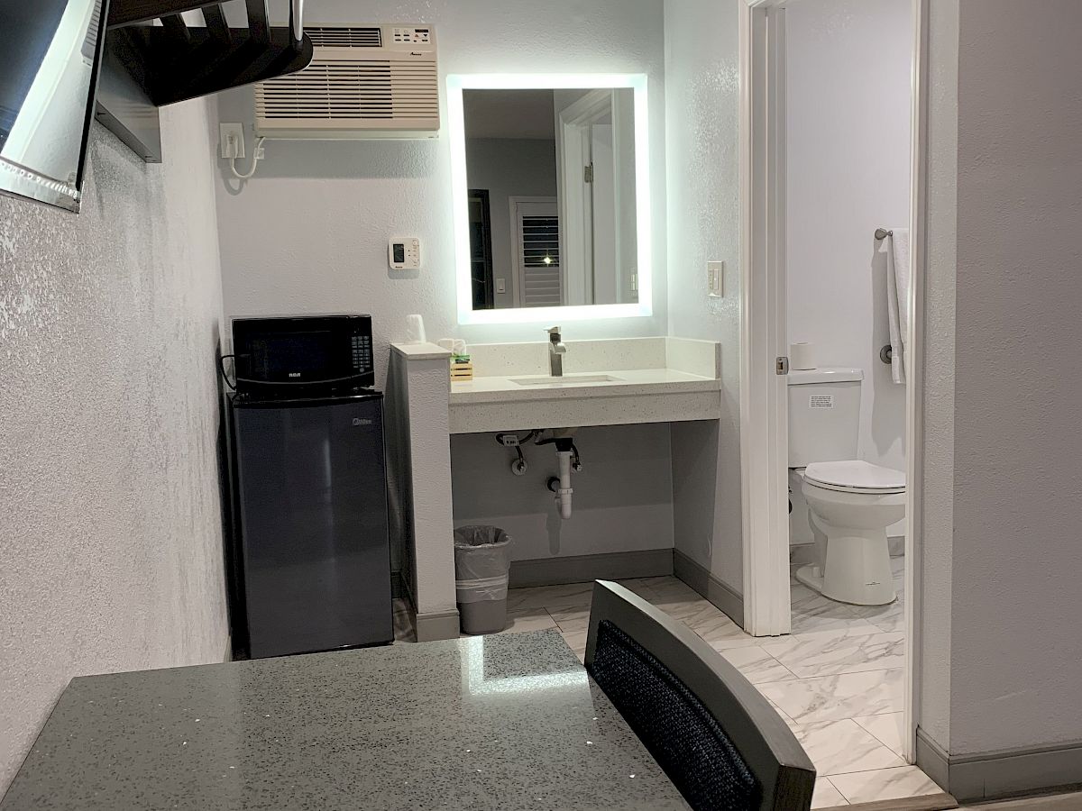 A small hotel room with a TV, mini-fridge, microwave, sink, desk, and a bathroom. The sink is outside the bathroom. There is also a chair.