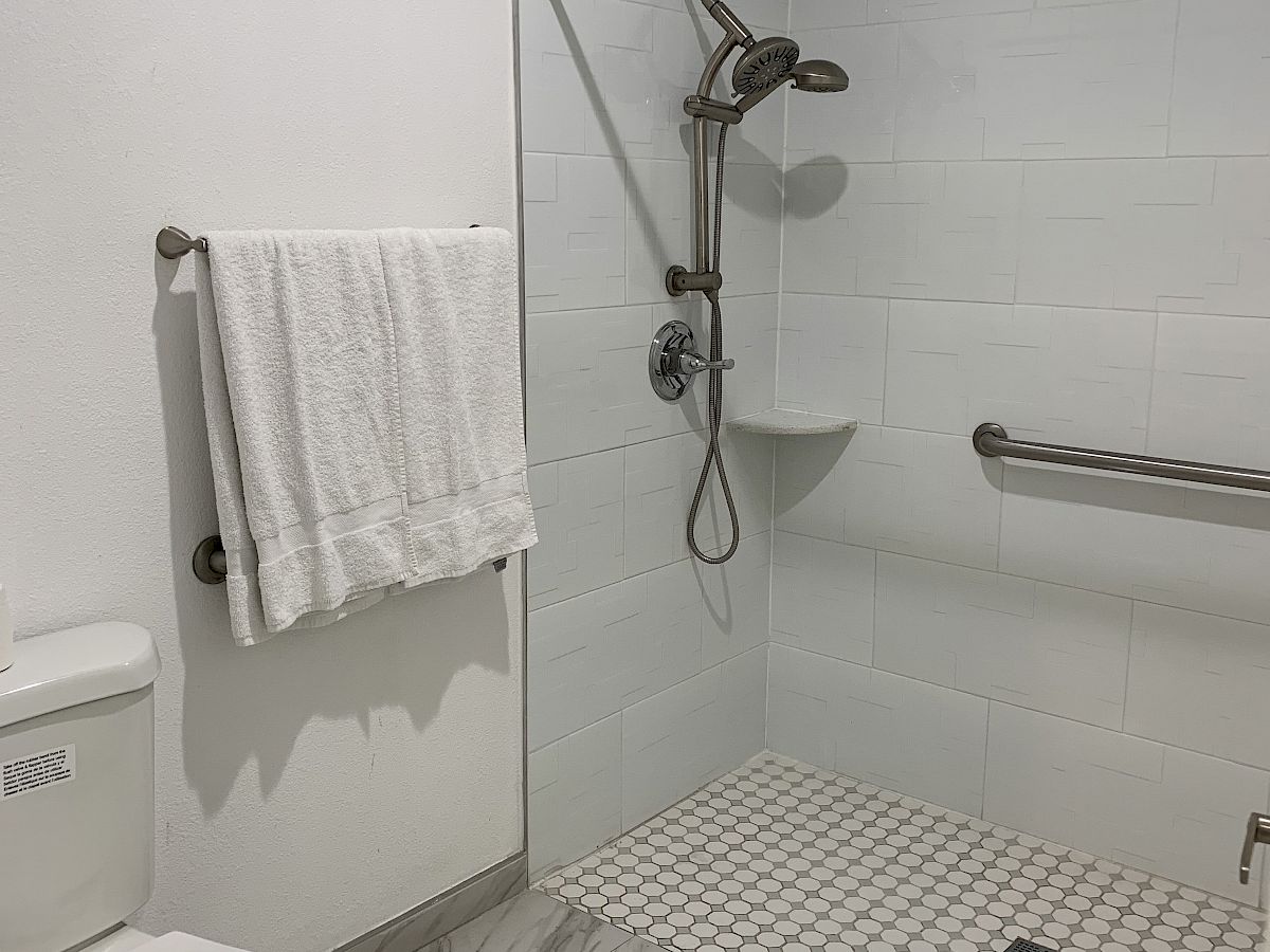 The image features a bathroom with a walk-in shower, toilet, towel on a bar, and marble-patterned floor tiles.