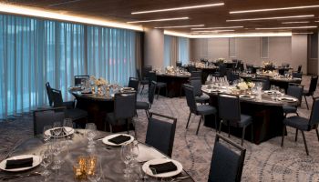 The image shows a well-decorated banquet hall with round tables, chairs, elegant table settings, and dim lighting, creating a sophisticated ambiance.