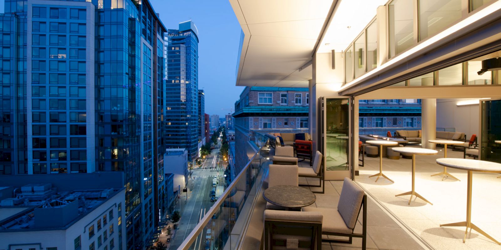 A modern balcony in a high-rise building overlooks a cityscape at dusk, with buildings and street lights illuminating the scene.