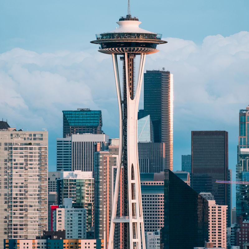 The image shows the Space Needle towering over the skyline of a city, likely Seattle, with various modern buildings in the background.
