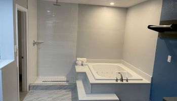 This image shows a modern bathroom with a large bathtub, a separate walk-in shower area, and tiled floors and walls.